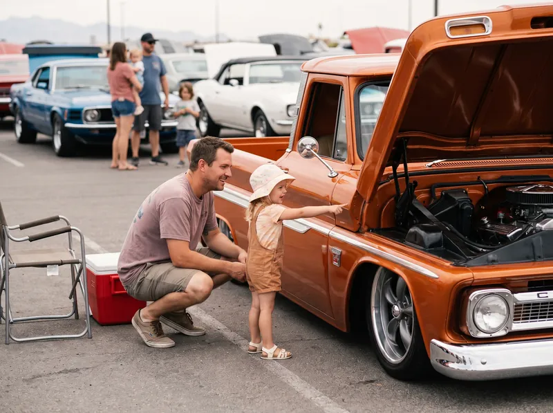 A dad and his daughter looking at an orange classic pickup at a car show